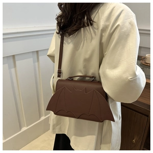 Close-up of a brown bat-wing shaped crossbody bag worn with a white coat for street style
