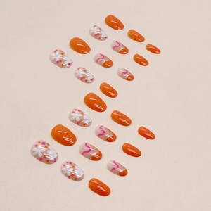 Short oval press-on nails with orange finish, white floral patterns and gold glitter detail
