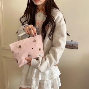 Detail of pink corduroy makeup bag with cute bear embroidery held by a model