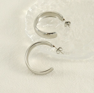 Gros plan sur des boucles d'oreilles C creuses en acier inoxydable argenté sur tissu