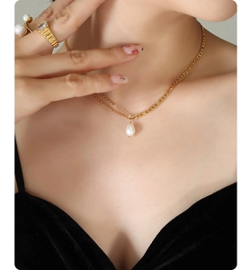 Close-up of double-layer gold chain necklace with pearl pendant on a model wearing velvet