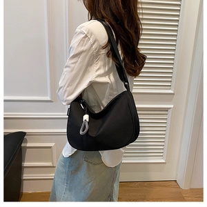 Detail of a black crescent nylon shoulder bag showing silver zipper and fashion tag