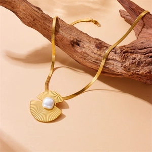 Gold snake chain necklace with fan-shaped pearl pendant displayed on a wooden branch