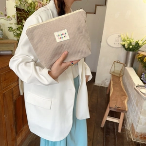 Detail of beige corduroy cosmetic bag with ozakka beauté embroidery held by a model