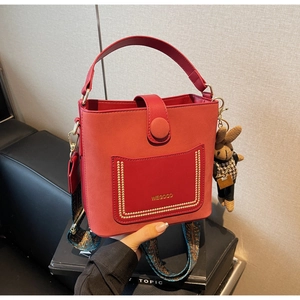 Detail of red leather bucket bag with wide ethnic strap and gold hardware accents