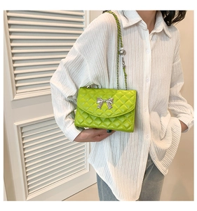 Detail of a bright green quilted crossbody bag with a silver metallic bow and chain strap