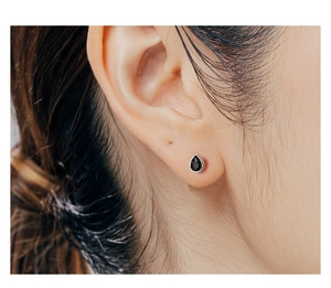 Macro shot of silver stud earring with black teardrop crystal on ear cartilage