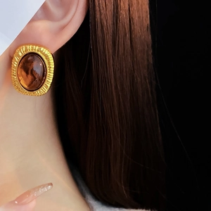 Close-up of vintage golden oval stud earring with amber resin center on model ear