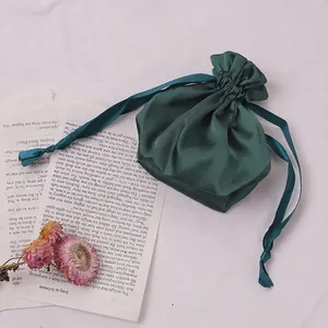 Dark green satin drawstring storage bag with silky ribbon on white textured fabric