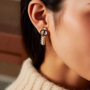 Close-up of gold-plated C-shaped earrings with pearls and crystals on a model's ear