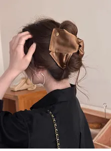 Détail d'une pince à cheveux en satin marron avec nœud portée par un mannequin élégant