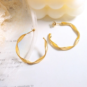 Twisted C-shaped 18K gold plated titanium earrings on a vintage book page