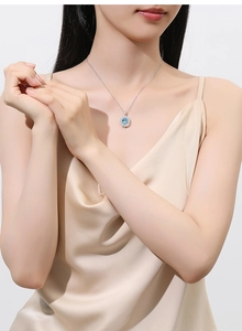 Detailed view of an oval blue gemstone necklace with sparkling diamond halo on a model