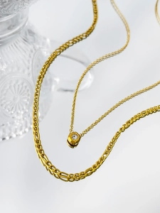 Detail of layered gold titanium steel necklace with curb chain and solitaire diamond pendant