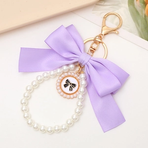 Detail view of purple ribbon bow keychain with white faux pearls and gold hardware