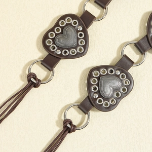 Detail of dark brown leather heart patches with silver rivets and woven rope tassels