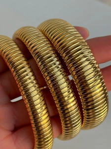 Close-up of three 18k gold plated stainless steel snake texture bangles held by hand