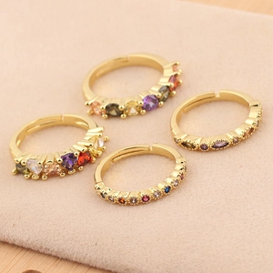 Detalle de cuatro anillos abiertos dorados con circonitas de colores en terciopelo rosa