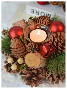 Close-up of vintage pine cone candle holder with red ornaments and glowing tea light