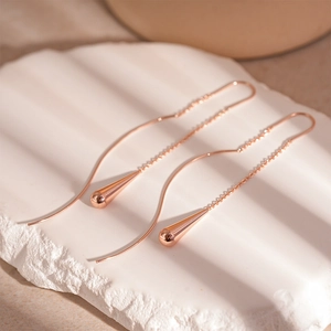 Detailed view of rose gold long water drop tassel earrings on white textured stone