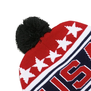 Detail of knitted USA flag beanie with stars, white text, and soft black pom-pom on top