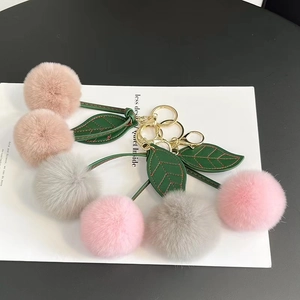 Macro detail of plush cherry keychain with soft fur poms and golden metal clasp