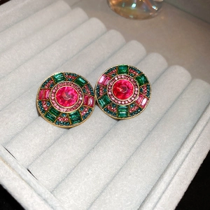 Detail of luxury gold stud earrings with red and emerald green crystals in a gray velvet box