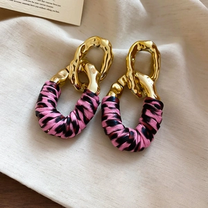 Detailed view of gold chain link earrings with pink and black leopard print leather wrapping