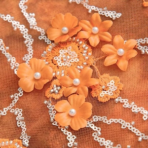 Detailed close-up of orange mesh fabric with floral appliques, white pearls and sequins