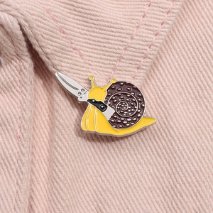 Close-up of cute snail enamel pin holding a knife on pink denim fabric texture