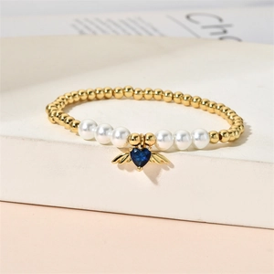 Detail showing a heart-shaped blue gem with golden angel wings on a beaded pearl bracelet