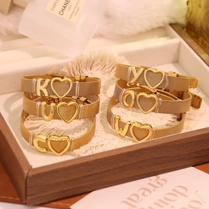 Détail du bracelet maille dorée avec breloques lettres et cœur sur plateau bois