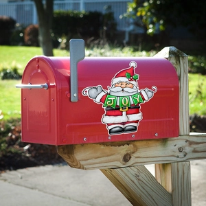 Red metal mailbox with Santa Claus Joy magnetic sticker on a grassy garden background