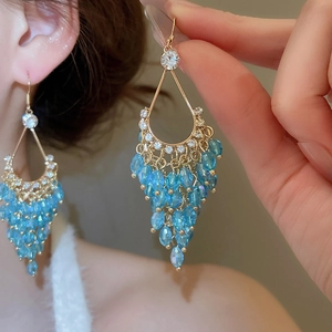 Detailed macro view of waterdrop-shaped gold tassel earrings with blue crystals and zircons