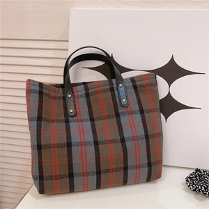 Detail of checkered canvas tote bag with black leather handles and gold rivet accents