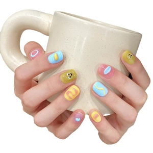Handmade 3D macaron press-on nails with cartoon eyes and wavy textures on a mug