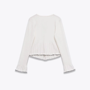 Detailed view of white knit top featuring black contrast piping and ruffled hem details