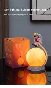 Close-up of floating astronaut moon lamp with warm glow and orange packaging box