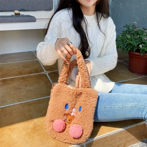Close-up of brown teddy fleece handbag featuring cute blush pom-poms and cartoon embroidery