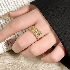 Gold plated snake ring with sparkling zircons and green gemstone eyes on finger