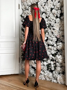 Rear view of a square-neck puff sleeve dress with cherry print against a white rose wall