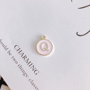 Detail view of round pink enamel pendant with gold metal letter Q for DIY jewelry making