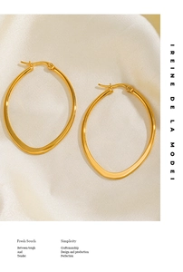 Close-up of polished golden oval hoop earrings on elegant beige silk fabric background