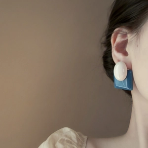 Close-up of geometric oval white and blue earrings worn by a model on a brown background