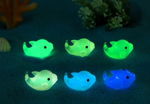 Luminous dolphin resin figurines glowing in green and blue colors on dark sand background