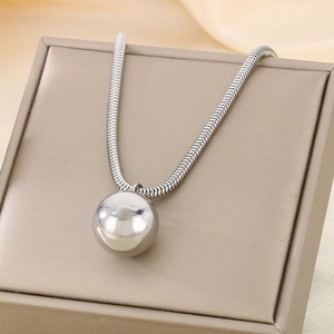 Detailed view of silver hollow ball pendant on snake chain over beige fabric
