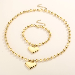 Polished gold beaded necklace and bracelet set with smooth heart pendants on beige background