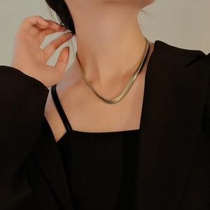 Close-up of a wide gold snake chain necklace on model neck showing smooth metal texture