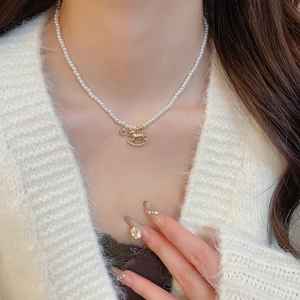 Detailed shot of pearl necklace with gold rocking horse pendant on a woman neck