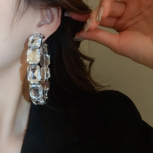 Detailed close-up of large silver C-shaped hoop earrings with square cubic zirconia stones